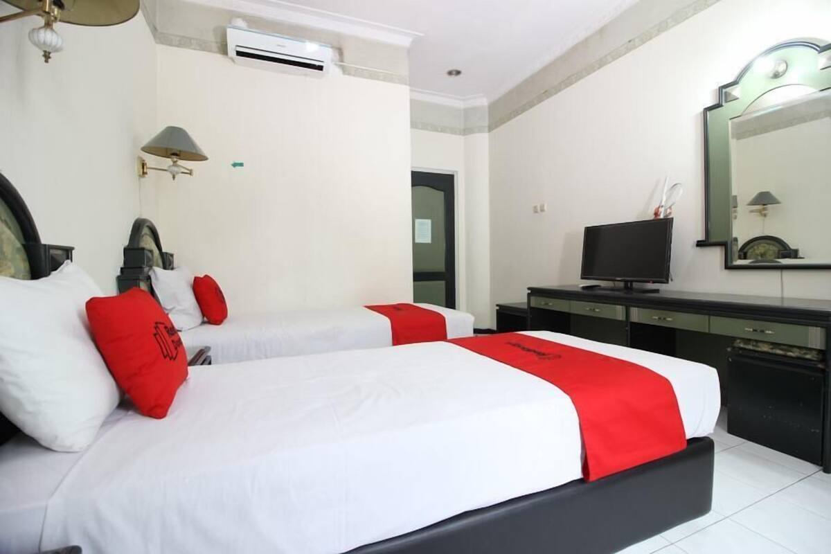 Quarto de hotel com duas camas, televisão, escrivaninha e espelho.
