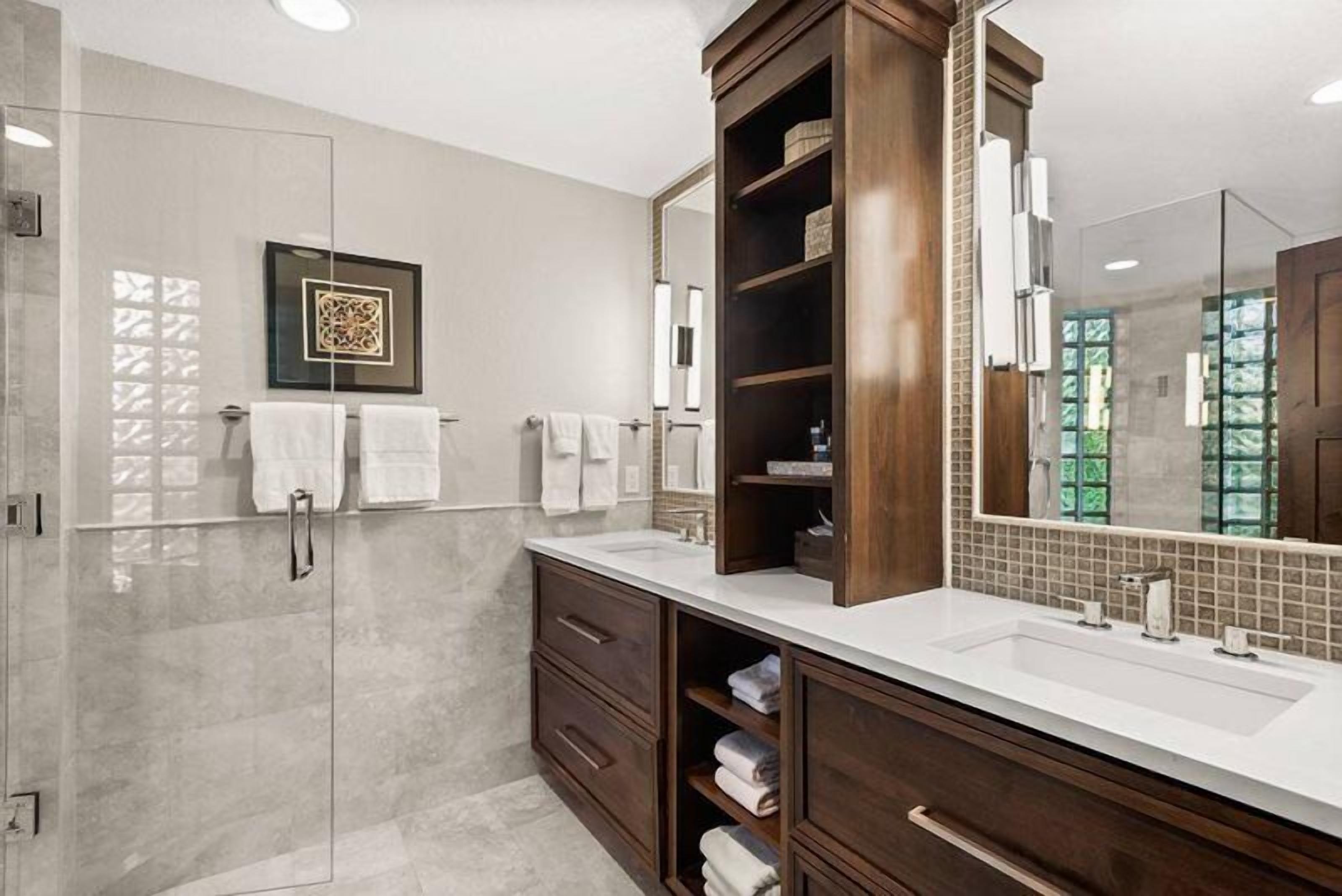 A modern bathroom with two sinks, a large mirror, and a walk-in shower.