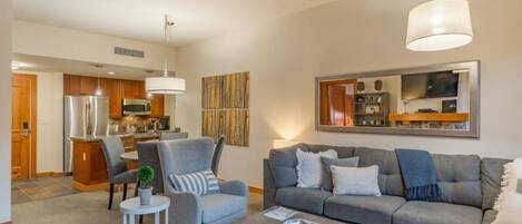En moderne stue med en grå sofa, et sofabord og et spiseområde med et køkken i baggrunden.