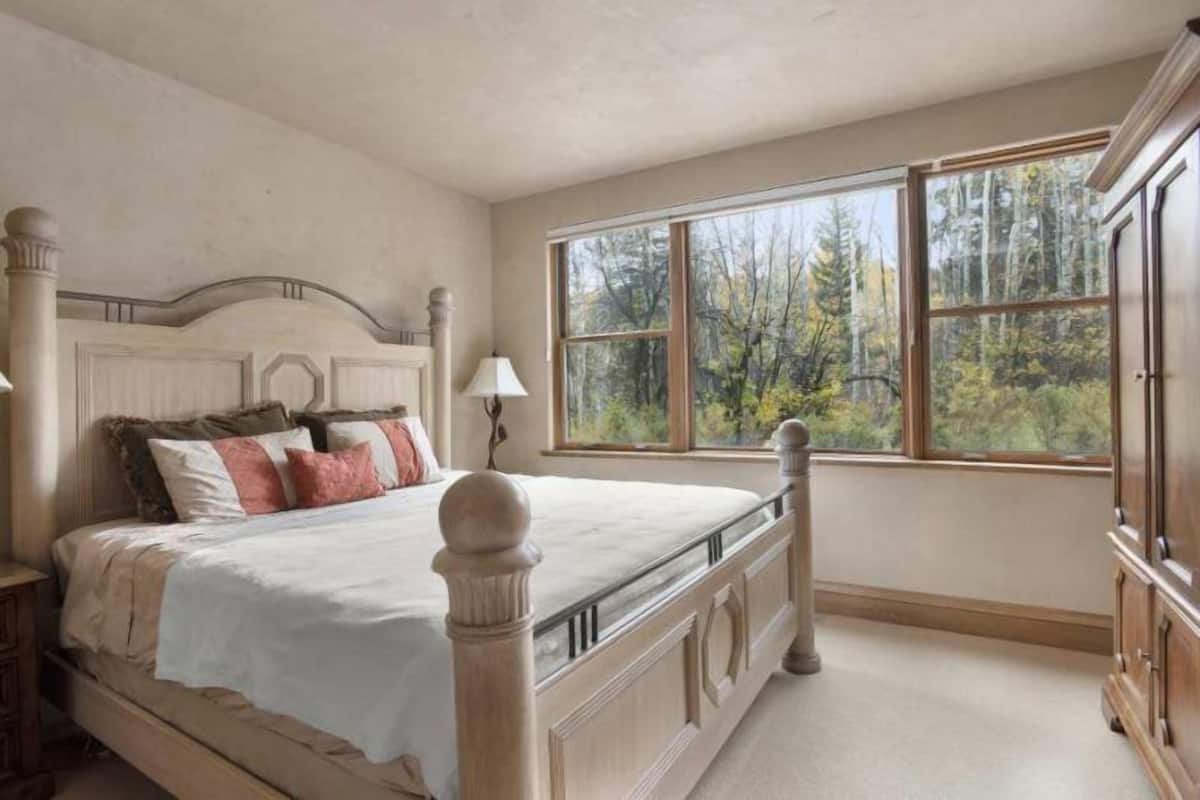 Un dormitorio con una cama grande, un ventanal con vistas a árboles y una mesita de noche de madera.