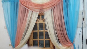 Een raam met houten kader en een decoratieve gordijnstelling in blauw, roze en crème tinten.