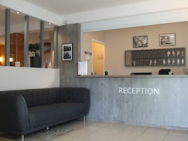 A reception area with a grey sofa, a reception desk labeled "RECEPTION," a wall-mounted key display, and a framed picture.