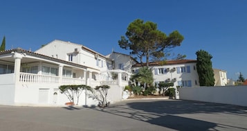 Un edificio blanco con balcón, un árbol grande y cielo despejado.