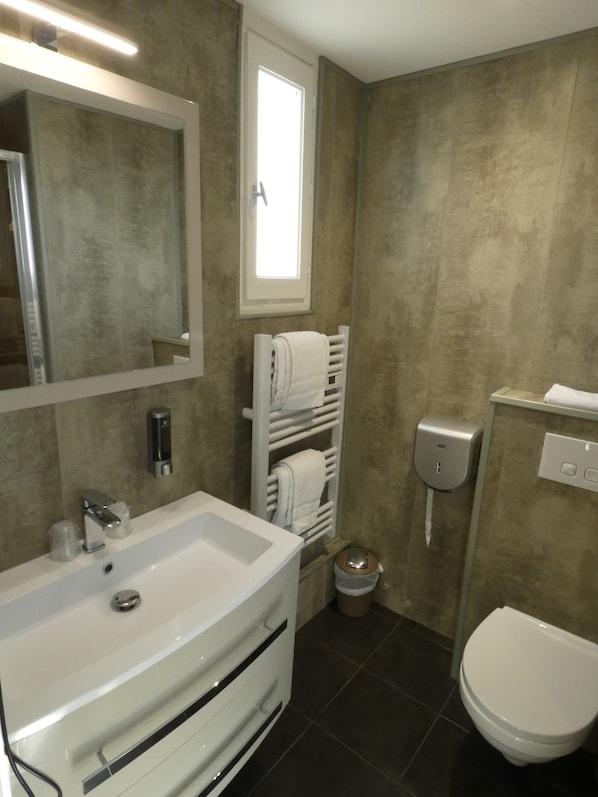 Un baño con lavamanos blanco, espejo, toallero y inodoro.