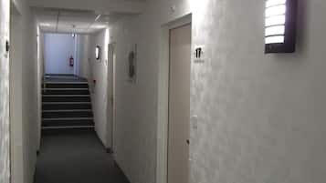 A hallway with a carpeted floor, a staircase at the end, and a wall-mounted light fixture.