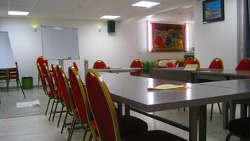 Un salón de conferencias con una larga mesa, sillas rojas, una pizarra y un cuadro en la pared.