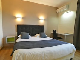 Habitación de hotel con una cama grande, dos lámparas de noche, un escritorio y un aire acondicionado.