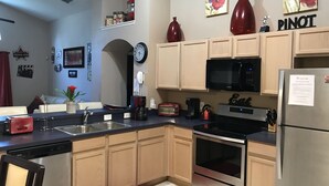 A modern kitchen with a dishwasher, microwave, stove, and refrigerator. There is a clock on the wall and a red vase on the counter. - 4BR 3BA Home in Rolling Hiils by CV-7901 (Kissimmee)