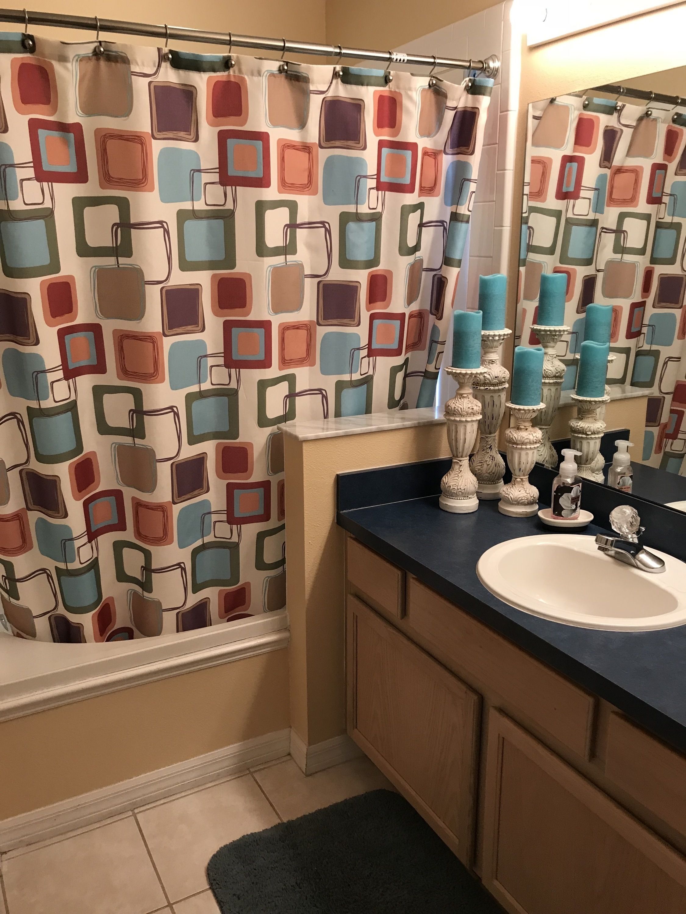 Un bany amb una cortina de dutxa estampada, un lavabo amb mirall i gerros decoratives a la superfície.