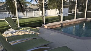 A pool area with green lounge chairs and a white fence in the background. - 4BR 3BA Home in Rolling Hiils by CV-7901 (Kissimmee)