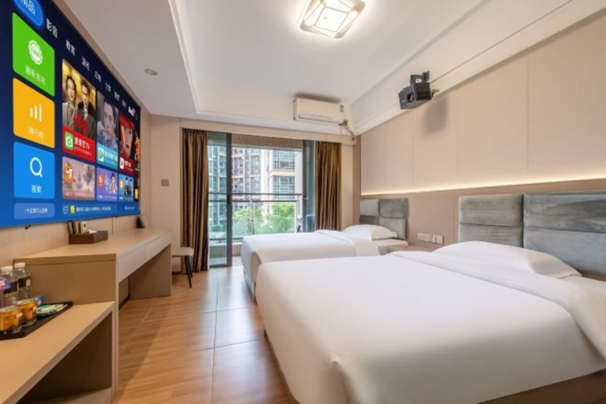 A hotel room with two beds, a desk with a computer, and a large digital screen displaying various apps.
