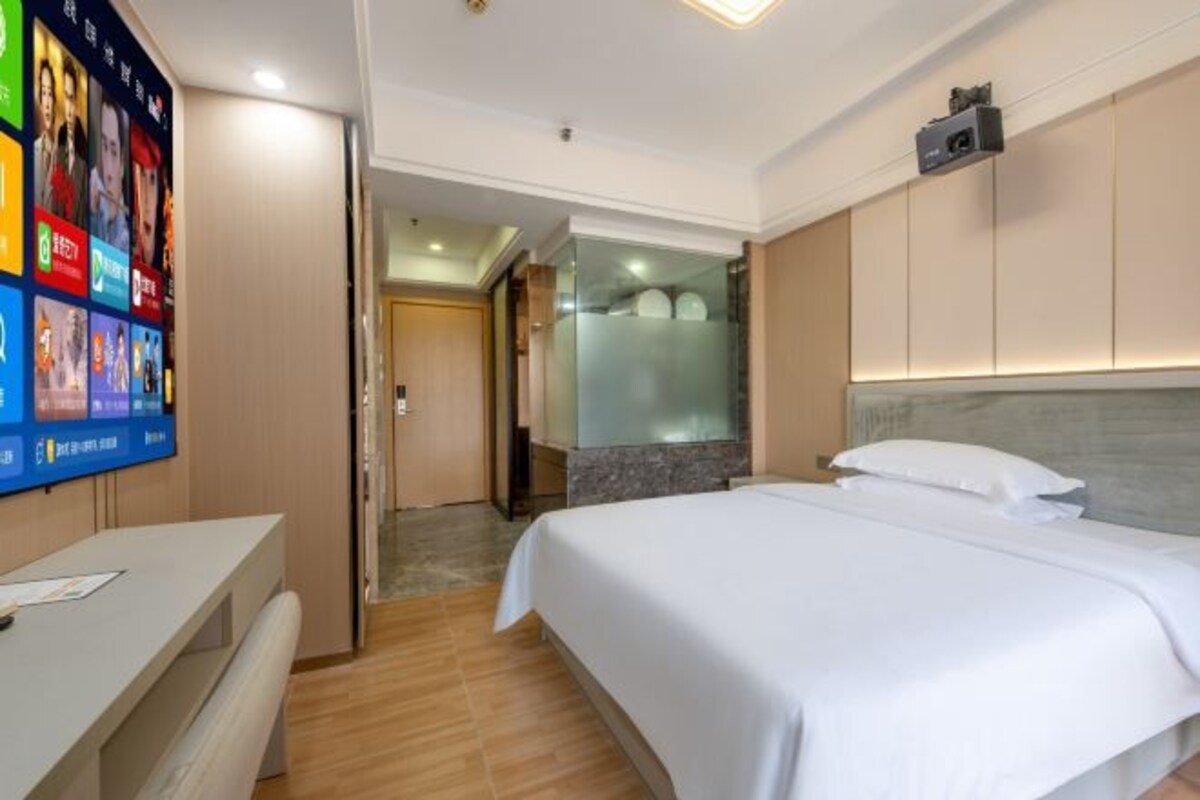 A hotel room with a bed, a desk, and a TV displaying various channels.