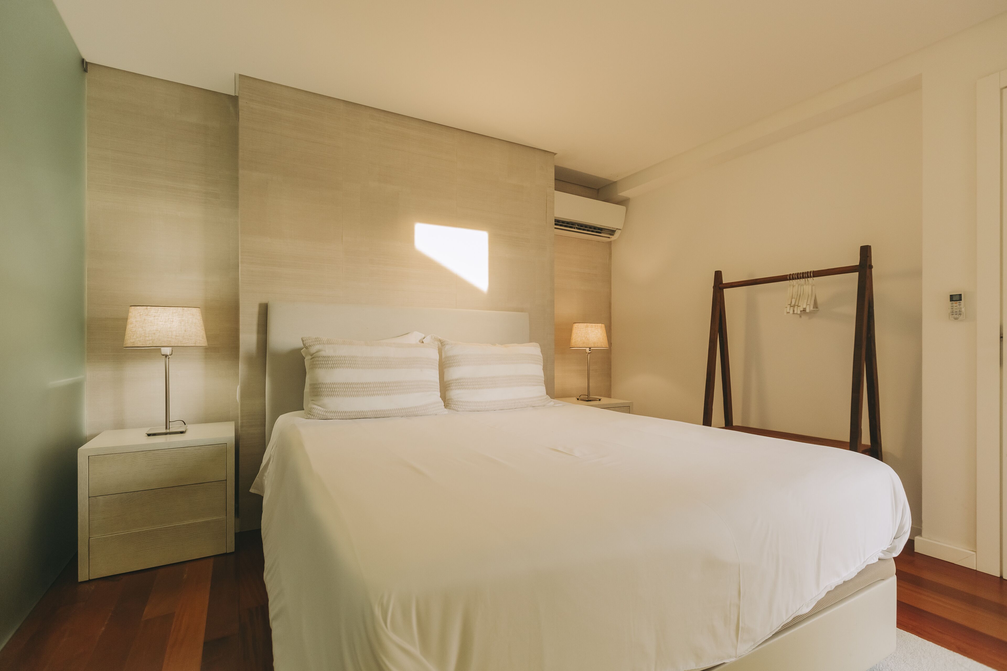 Un dormitorio con una cama grande, dos mesitas de noche con lámparas, un armario de madera y un perchero.