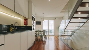 A modern kitchen with white cabinets, a black countertop, and a dining area with a glass table and chairs. - Ocean Views by Azores Villas (Ponta Delgada)