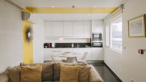 A modern kitchen with white cabinets, a dining table with chairs, and a yellow accent wall. - Ocean Views by Azores Villas (Ponta Delgada)
