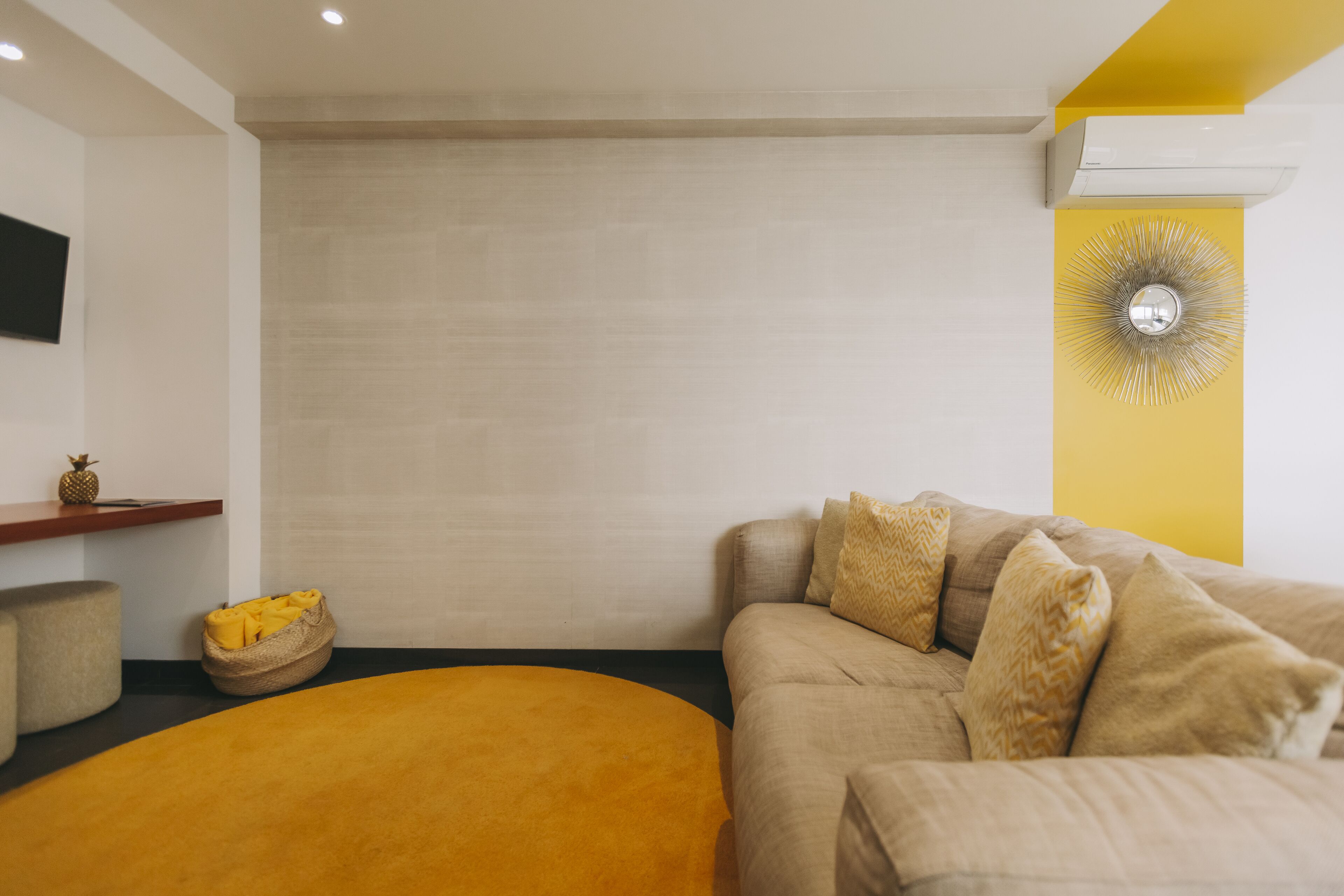 A modern living room with a beige sofa, a yellow ottoman, and a wall-mounted air conditioner.