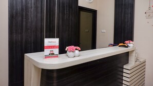 Una mesa de recepción con un reloj, un cartel y dos jarrones con flores rosas.