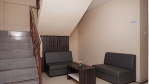 Un interior moderno con una escalera, dos sofás grises, una mesa de centro de madera y un pequeño jarrón con flores.