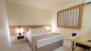Habitación de hotel con cama, mesita de noche, lámpara y un pequeño escritorio con silla.