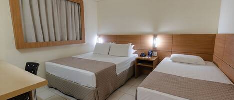 A hotel room with two beds, a desk, and a window with curtains.