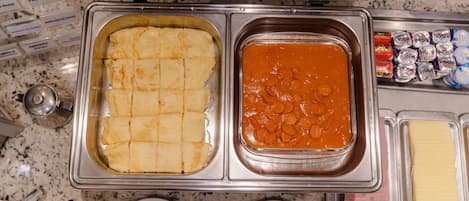 Un bufé con dos platos principales: una bandeja de papas en cubos y un recipiente con salsa de tomate.