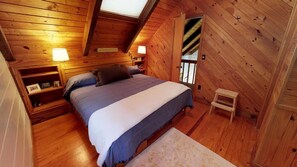 Une chambre confortable aménagée dans un chalet en bois, avec un lit, des lampes de chevet, un petit tabouret et une étagère où sont posés des objets personnels.