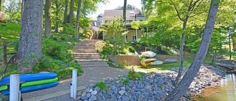 A wooden deck leading to a house surrounded by trees and a small stream.