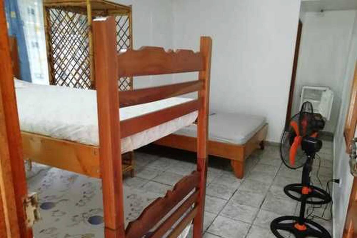 A small room with a wooden bunk bed, a small table, and a standing fan.