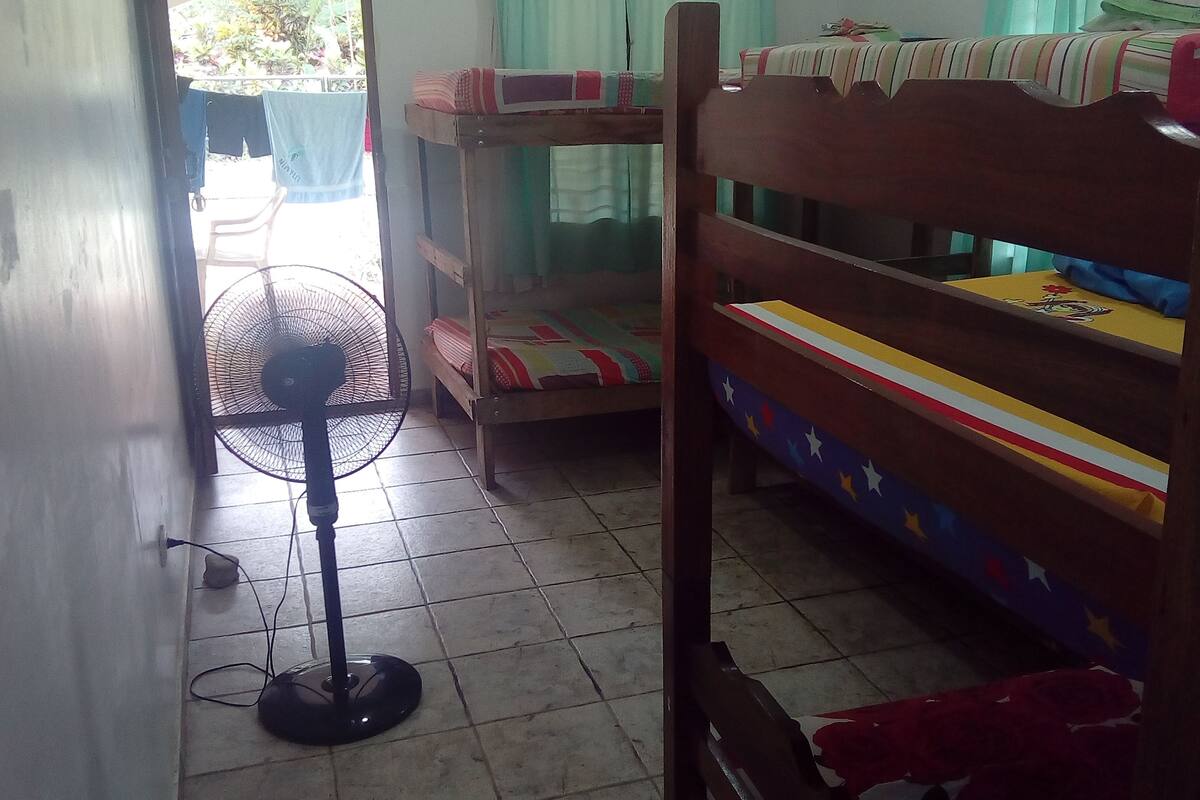 A dormitory room with bunk beds, a standing fan, a tiled floor, and a door leading outside.