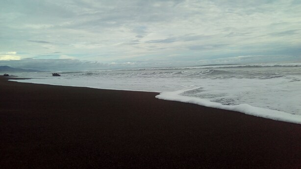 Une plage au sable sombre, bordée par des vagues.