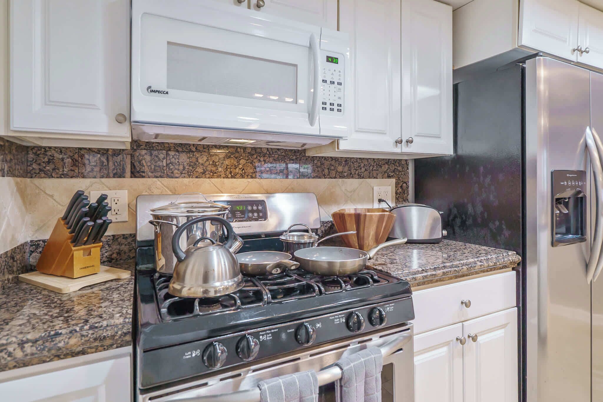 A kitchen with white cabinets, a stainless steel stove, a microwave, and a refrigerator.
