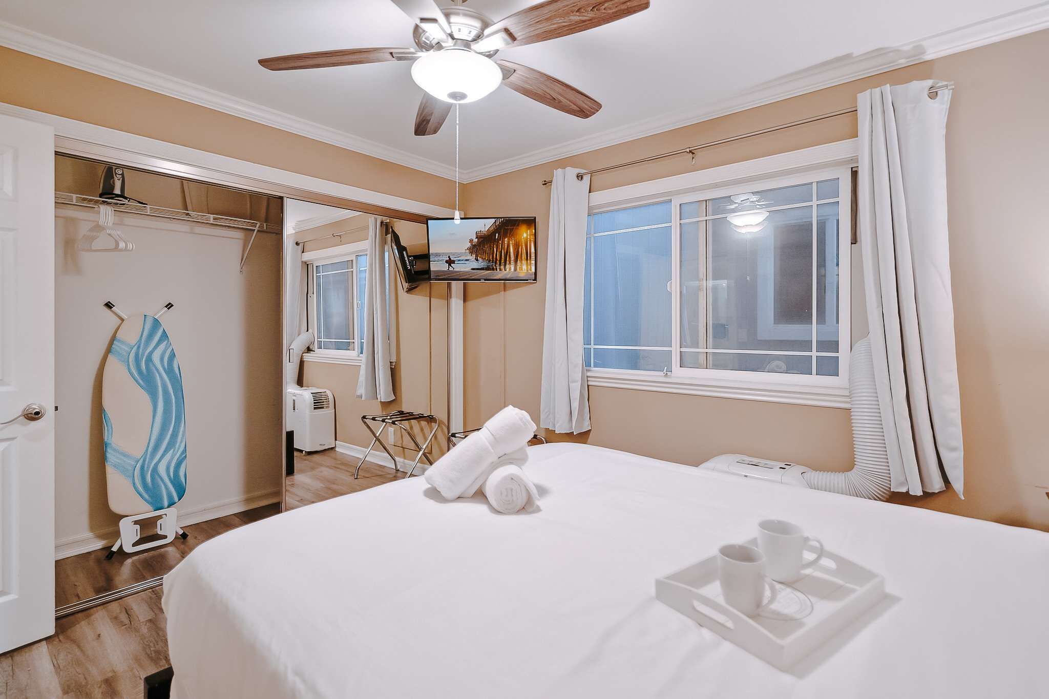 A hotel room with a bed, a ceiling fan, a TV, a window with curtains, a towel rack, and a mirror.