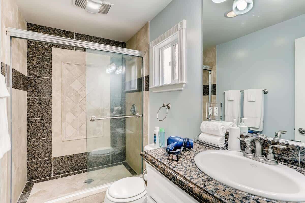 Un baño moderno con ducha de vidrio, lavamanos con encimera de granito y un espejo grande.