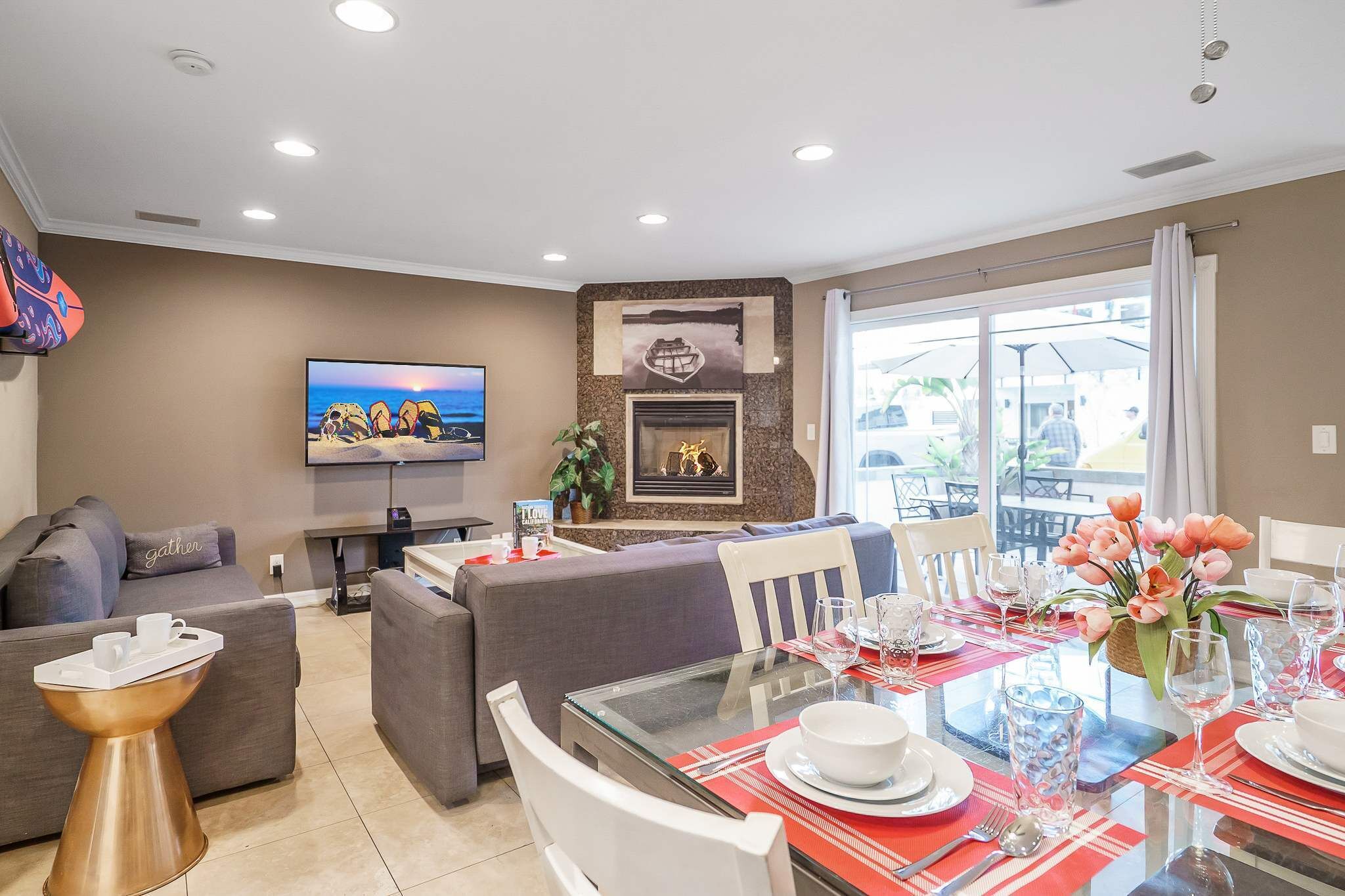 A modern living room with a fireplace, a dining area set for a meal, and a large TV on the wall.