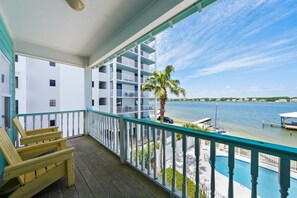 A balcony with a view of a lake, a pool, and a palm tree.
