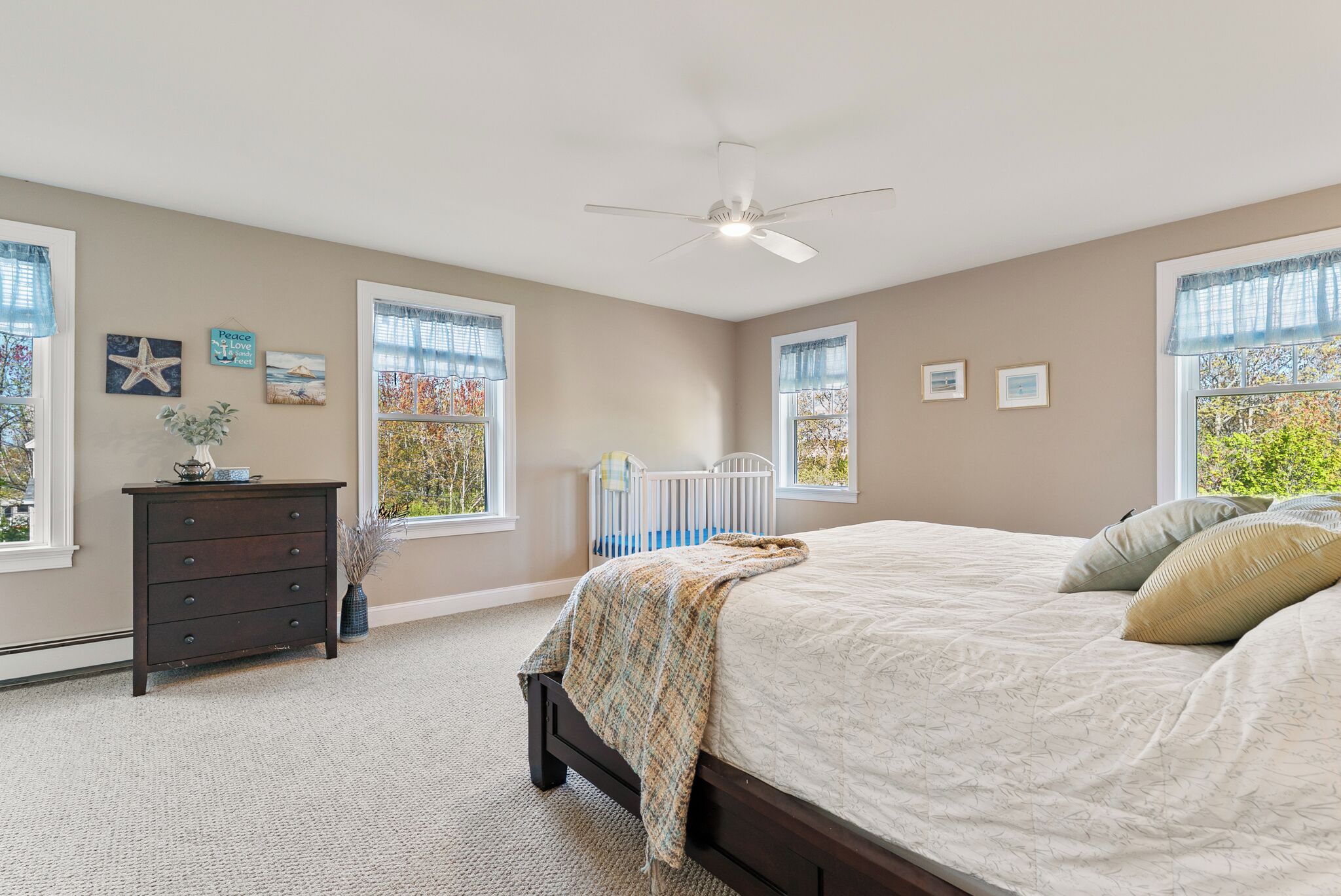 Une chambre à coucher avec un lit, une commode, des fenêtres et un ventilateur de plafond.