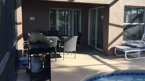 A patio area with a pool, a table with chairs, and a grill.