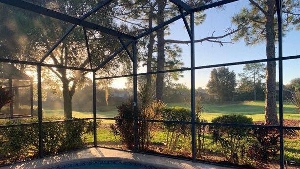 A pool area with a view of a golf course through a glass enclosure.
