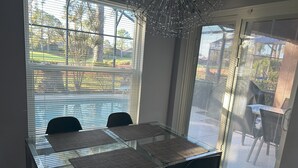 A dining area with a glass table and chairs, a decorative chandelier, and a view of a landscaped garden through large windows.