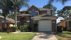 A two-story residential house with a garage, a front yard with grass and shrubs, and a clear blue sky.
