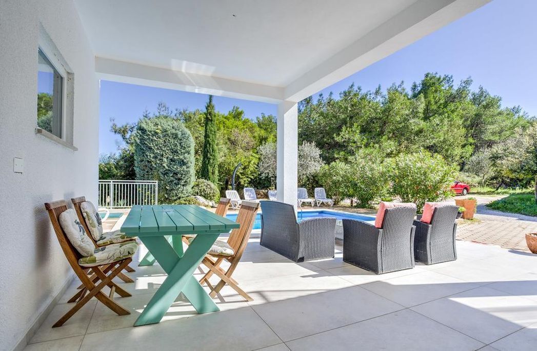 A covered outdoor patio with a pool, lounge chairs, and a dining table.