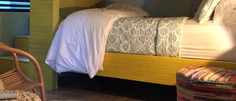 Un lit superposé avec un lit en bas, un lit simple, un pouf en osier, une chaise en bois et un petit tapis.