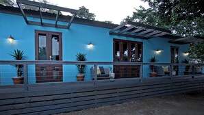Un edificio azul con terraza de madera, plantas en macetas y mobiliario exterior.