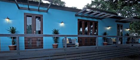 Un bâtiment bleu doté d’une terrasse en bois, de plantes en pot et d’un espace salon extérieur.