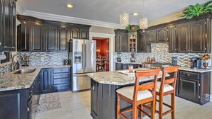 A spacious kitchen with dark cabinetry, granite countertops, and a central island with bar stools.