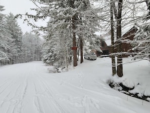 A snow-covered road with a vehicle parked by a building.