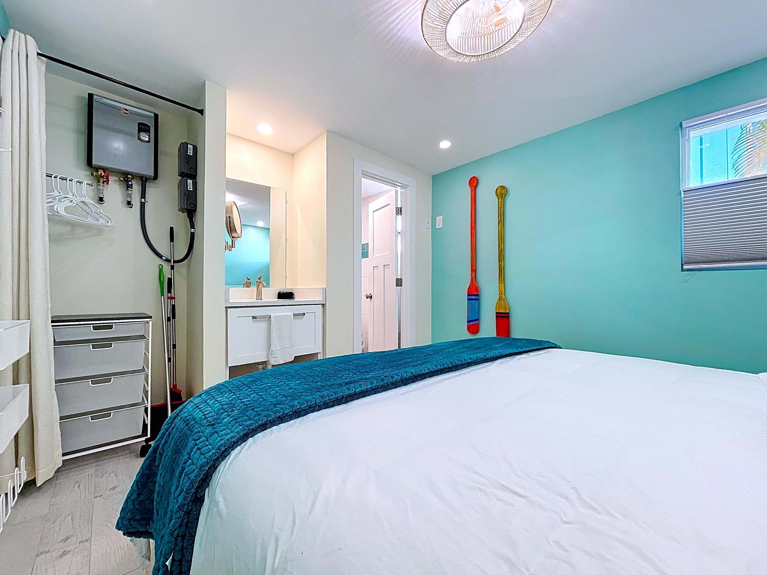 A bedroom with a bed, a desk with drawers, a mirror, a window, and a ceiling light fixture.