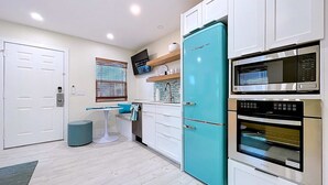 Una cocina compacta con armarios blancos, un refrigerador verde azulado, un microondas y un horno empotrado.