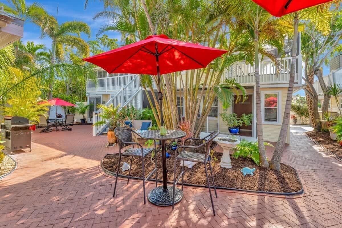 A patio area with a round table and chairs, surrounded by palm trees and a red umbrella.