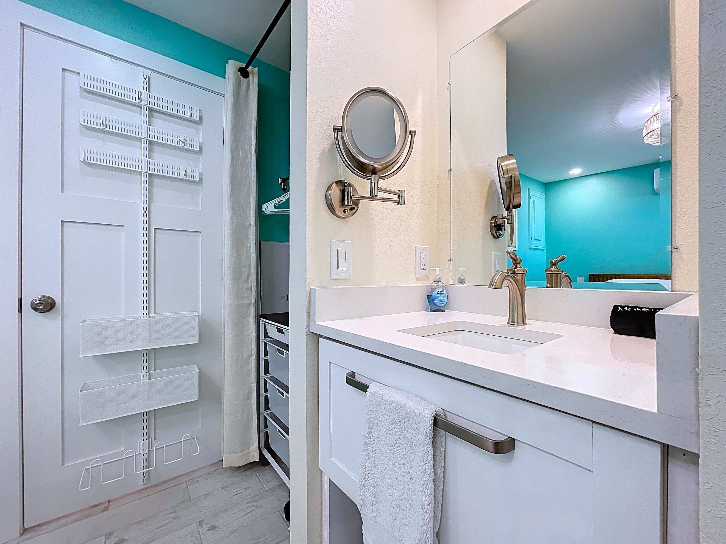 A bathroom with a white sink, a mirror, a towel rack, and a door with a towel hanging on it.